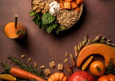 Bol composé de légumes rôtis, pois chiches, quinoa, noix et sauce crémeuse, entouré de légumes et courges d’automne disposés sur une table marron.