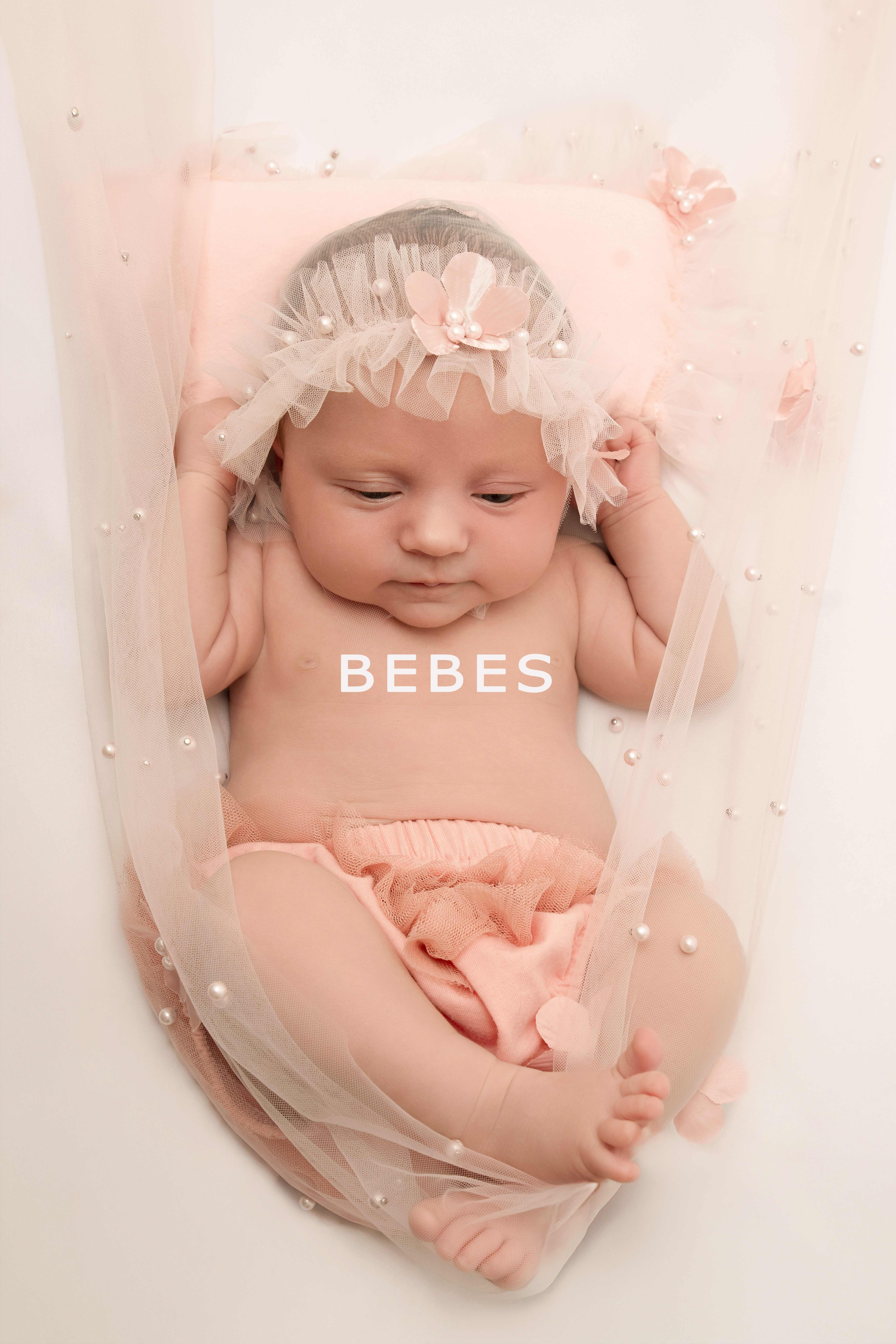 Photographie de nouveau-né -bébé en studio Photographie de nouveau-né réalisée en studio, bébé allongé sur un fond rose poudré avec accessoires en tulle et perles, capturée par un photographe professionnel spécialisé dans les séances bébé.