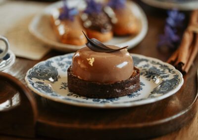 Photographie culinaire d’un dessert au chocolat brillant orné d’une feuille en chocolat et de touches dorées, présenté sur une assiette en porcelaine, dans une ambiance élégante et chaleureuse. Réalisée par un photographe culinaire professionnel spécialisé en pâtisserie fine.