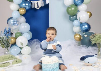 Séance cake smash en studio avec un bébé célébrant son premier anniversaire dans un décor marin aux tons bleus et verts, photographié par un photographe professionnel spécialisé dans les séances photo bébé.