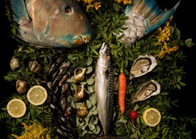 Photographie culinaire artistique représentant une nature morte marine composée de poissons, coquillages et huîtres, accompagnés de citron et de végétation, réalisée par un photographe culinaire professionnel dans une ambiance sombre et graphique.